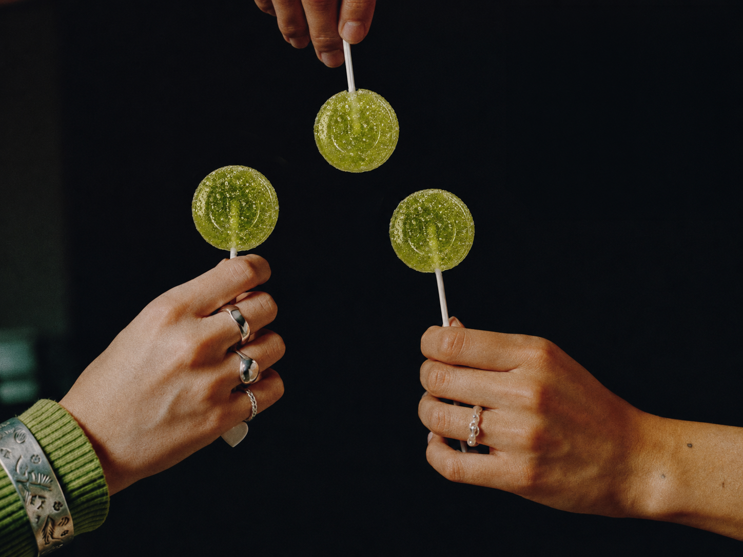 Three hands holding green lollipops